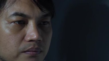 Ciddi, dalgın ya da hüzünlü bir ifadeyle Asyalı bir adamın aşırı yakın portresi. Hafif ışıklandırma cilt dokusunu, gözleri ve yüz hatlarını vurguluyor. 4K çözünürlüğündeki duygusal depresyon, yorgunluk veya derin düşünme kavramı.