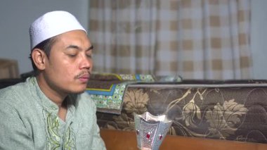 Geleneksel giysiler içinde Müslüman Asyalı bir adam ve kopya evde bir fırın kullanıyor. Koku ve rahatlama için tütsüden duman çıkarmak. Otantik İslami yaşam tarzı, ruhani gelenek ve Ortadoğu tütsü kültürü kavramı.