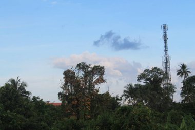Yüksek bir telekomünikasyon kulesi ya da açık mavi gökyüzünün altında yemyeşil bir orman tepe örtüsünün üzerinde duran bir telefon sitesi. Uzak ya da kırsal bölgelerdeki bağlantı, dijital teknoloji ve kablosuz iletişim altyapısını sembolize eder.