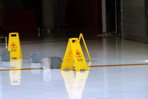 Yellow caution wet floor signs stand next to gray buckets on the tiled floor