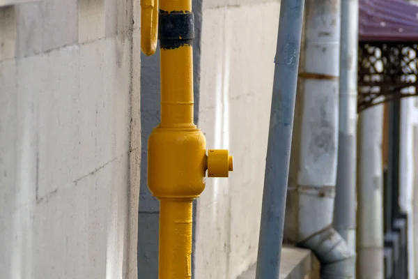 Yellow gas pipe to provide a residential building near a wall next to other pipes