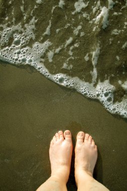 Kumun üzerinde çıplak ayaklar ve yanında dalgalar..