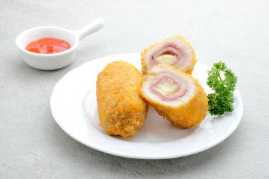 Çıtır Cordon Blue, jambon ve peynirli tavuk fileto. Gri arkaplanda beyaz plaka ile servis edilir. 