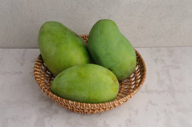 Gri arka planda rattan sepetinde taze ve olgun mango meyvesi servis edilir. Kapat..