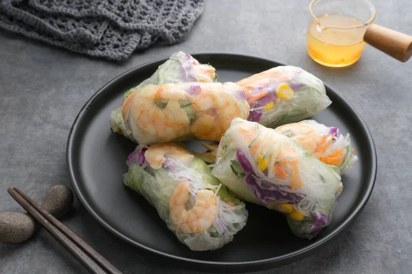 Vegetable spring roll, fresh roll salad made from mix vegetables and shrimp. Served in black plate on dark concrete background. Selective focus image.