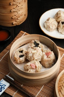 Bambu buharı ve baharatlı sosta servis edilen çeşitli malzemeli Dimsum. Tahta masada servis edilir..