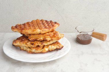 Bir yığın Karamelli Kruvasan Waffle veya Croffle gri arka planda beyaz tabakta servis edilir. Kapat, boşluğu kopyala.