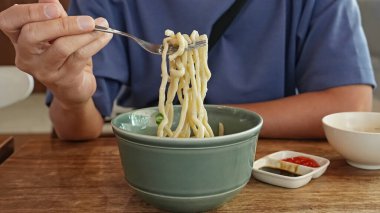 Bir adam kafede laksa erişteli erişte yiyor ve tadını çıkarıyor.