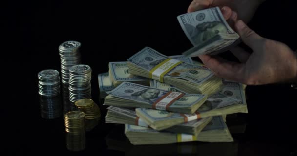 Een hand gooit geld over stapels geld, goud en munten. — Stockvideo