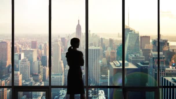 マンハッタンのスカイラインでオフィスの窓の外を見るシルエットの女性 — ストック動画