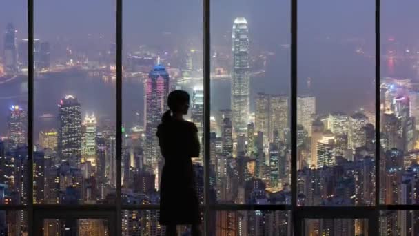 Une femme Silhouette regardant par la fenêtre du bureau à hong kong horizon de la nuit — Video