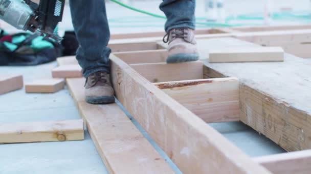 Un trabajador de la construcción masculino usando una pistola de clavos en el marco de madera del perno en un sitio en desarrollo — Vídeo de stock