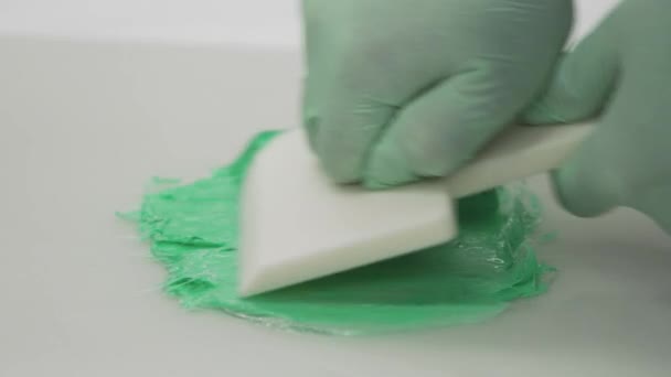 Unas manos con guantes usando un cepillo de espuma para mezclar pintura verde en plástico transparente en el banco de trabajo — Vídeos de Stock