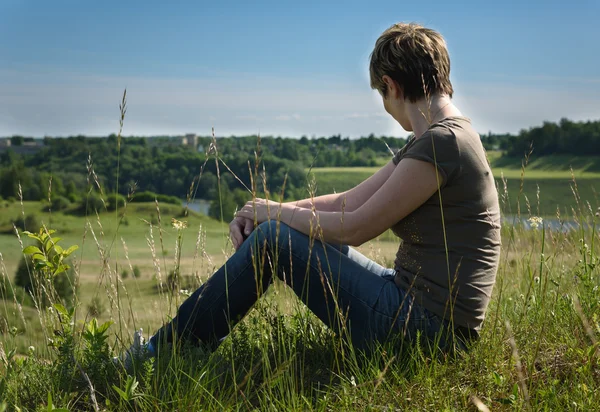 Femme solitaire assis avec son dos sur le champ vert — Photo