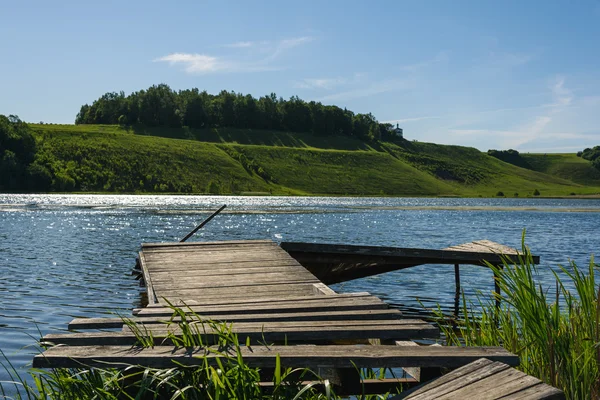 Viejo embarcadero de madera en el lago de primavera sobre fondo de cielo azul — Foto de Stock