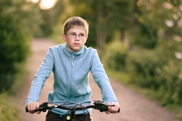 Menino adolescente com óculos em passeios de bicicleta ao longo de uma estrada rural — Fotografia de Stock