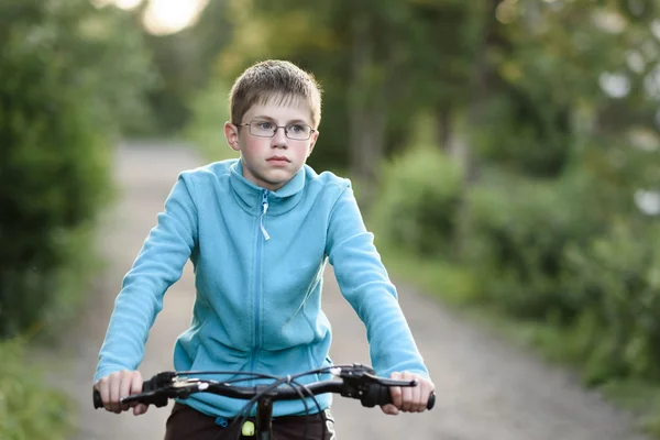 Adolescent garçon avec des lunettes sur des promenades à vélo le long d'une route de campagne — Photo