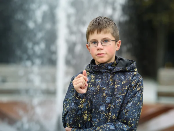 Sério menino adolescente de pé em um parque no fundo da fonte — Fotografia de Stock