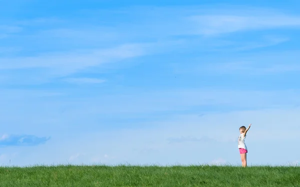 Happy little girl standing in a field on blue sky background — Stock Photo, Image