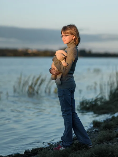 Дівчина підліток стоїть з іграшкою і дивиться на захід сонця на озері — стокове фото