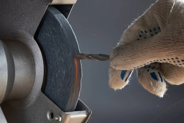 Sharpening drill. The hand wearing a work glove of man regrinding the drill tool for sharpen the drill tool with grinding wheel. Royalty Free Stock Images