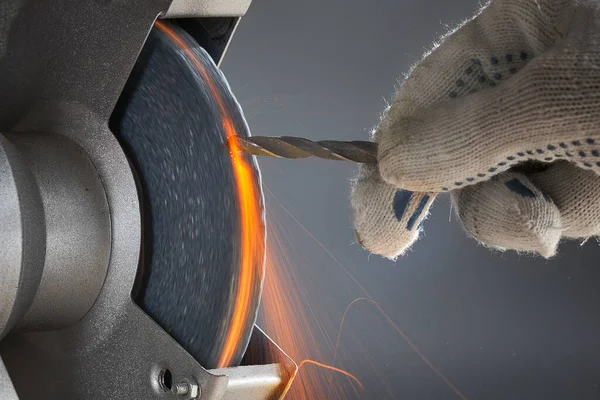 The hand wearing a work glove of man regrinding the drill tool for sharpen the drill tool with grinding wheel. The grinding wheel is hot and a lot of sparks. Stock Photo