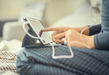 Ev kıyafetleri içinde bir kız yatağa oturmuş not defterine not alıyor. Evde çalışma kavramı..