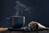 Fotografie s místem pro kopírování. Šálek horkého čaje s párou a sáček čajových sáčků na dřevěném stole na černém pozadí.
