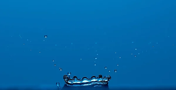 Rent klart vatten stänk som en krona isolerad på blå bakgrund. — Stockfoto