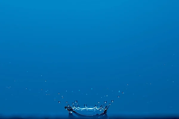 Puro respingo de água clara como uma coroa isolada no fundo azul. Foto com espaço de cópia. — Fotografia de Stock