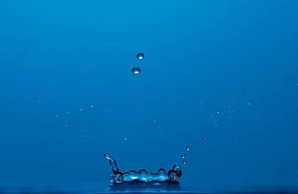 青い背景に隔離された王冠のような純粋な澄んだ水のスプラッシュ。コピースペース付きの写真. — ストック写真