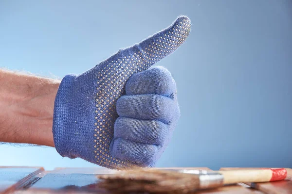 Main portant un gant de travail bleu avec pouce sur fond bleu et sur fond de surface en bois peint. — Photo