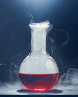 Kırmızı bir sıvıyla dikey cam şişe görüntüsü mavi arkaplanda buharlaşıyor..