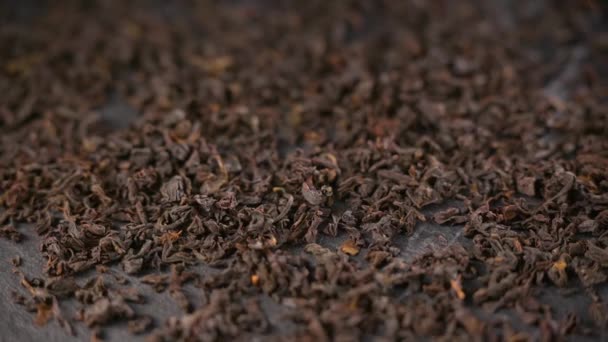 Las hojas secas de té negro se cierran. Té negro seco se dispersa en la mesa oscura. — Vídeo de stock