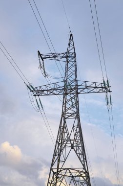 Mavi gökyüzüne karşı elektrik direkleriyle yüksek voltajlı elektrik hatları.