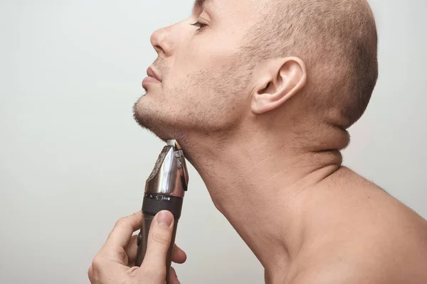 Imagen recortada vista lateral de un joven barbudo usando afeitadora eléctrica aislada sobre fondo gris. —  Fotos de Stock