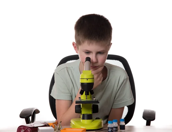 Menino adolescente olhando através de microscópio no fundo branco — Fotografia de Stock