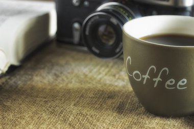 Eski kamera ve bir fincan kahve krematoryum ve kahve çekirdekleri çuval bezi tuval üzerine ahşap bir masa üzerinde yatan eski ders kitabı. Yakın çekim. 