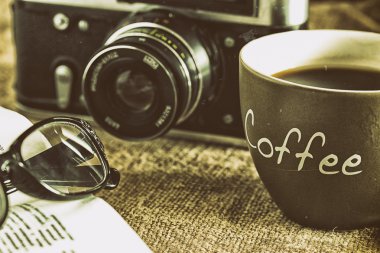 Eski kamera ve bir fincan kahve krematoryum ve kahve çekirdekleri çuval bezi tuval üzerine ahşap bir masa üzerinde yatan gözlüklü eski ders kitabı. Yakın çekim. Retro tarz