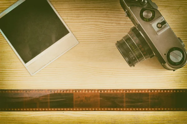 The camera and photograph with tape film lie on a wooden background. A collage of memories on film. Top view. Retro styled