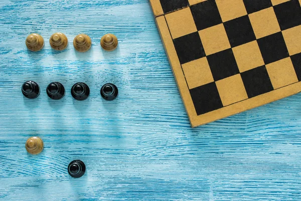 Παλιά περικομμένη σκακιέρα με μαύρο και άσπρο πιόνια σε μπλε φόντο ξύλινη. Κάτοψη. Lay επίπεδης. — Φωτογραφία Αρχείου