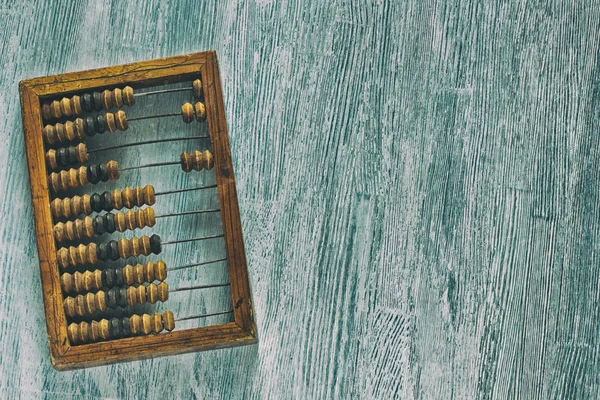 Old wooden scratched vintage decimal abacus on a blue wooden board for the background. Top view. Flat lay. Crop. The style of the old scratched photo with noise — Stock Photo, Image