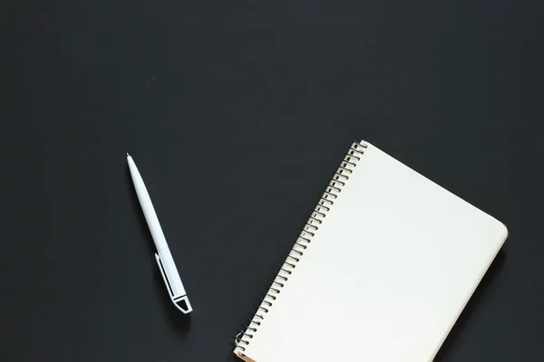 Un simple bloc-notes blanc vide avec un blanc pour le dessin ou l'écriture et un stylo en plastique blanc sont sur un bureau à partir d'un tableau noir. Vue de dessus. Maquette. Pose plate — Photo