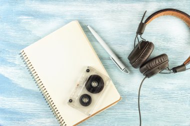 Müzik çalmak için büyük Vintage Deri kulaklıklar, mavi ahşap arka plan üzerinde tükenmez kalem ve ses bandı ile boş bir dizüstü bilgisayarın yanında yer almaktadır. Dalga geç. Üst te. Düz yatıyordu.