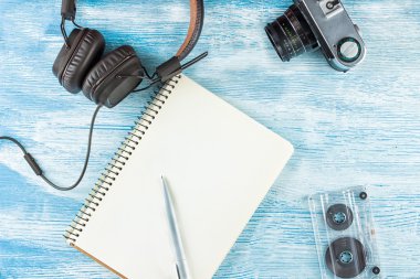 Müzik çalmak için büyük Vintage Deri kulaklıklar bir tükenmez kalem, fotoğraf kamera ve mavi ahşap arka plan üzerinde ses bandı ile boş bir dizüstü yanında yalan. Dalga geç. Üst te. Düz yatıyordu.