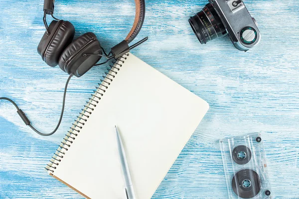 Müzik çalmak için büyük Vintage Deri kulaklıklar bir tükenmez kalem, fotoğraf kamera ve mavi ahşap arka plan üzerinde ses bandı ile boş bir dizüstü yanında yalan. Dalga geç. Üst te. Düz yatıyordu.