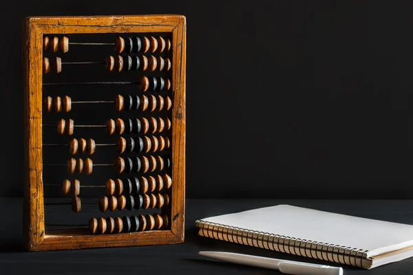 Alter aus Holz zerkratzter Vintage-Dezimalabakus, Stift und leerer Notizblock auf einem schwarzen Schreibtisch aus Kreidetafel mit Leerzeichen zur Beschriftung für den Hintergrund. Attrappe — Stockfoto