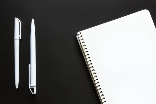 Tek basit boş beyaz defter ile boş bir çizim veya yazma ve beyaz plastik kalem için siyah kara tahta bir masaüstünden vardır. Üstten Görünüm. Mockup. Düz yatıyordu