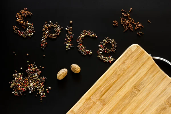 Food background. Spice written pepper, carnation, nutmeg and empty cutting board with blank space for mock up on black chalkboard. Topview. Mockup. Flatlay. — Stock Photo, Image