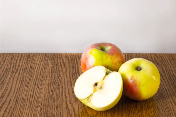 Dos manzanas enteras y media tumbadas sobre una mesa de madera — Foto de Stock